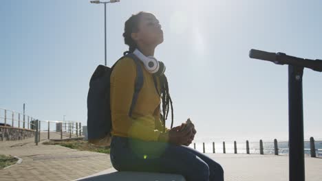 african american woman sitting eating sandwich promenade by the sea