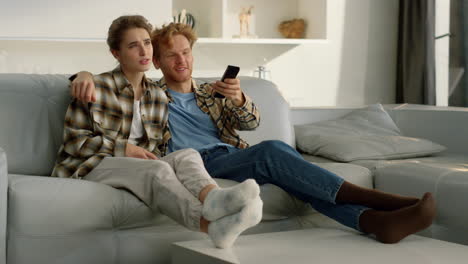 couple enjoy tv evening on comfortable sofa. happy ginger man embracing girl