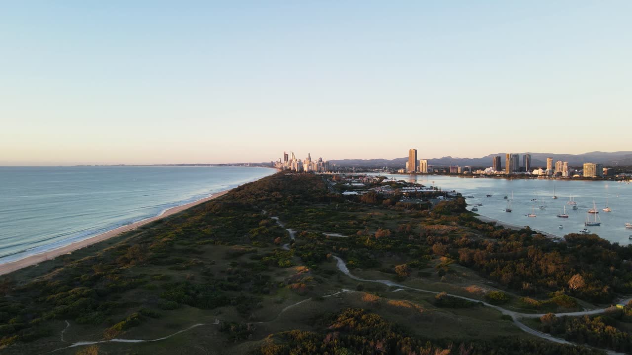 Coastal nature parklands dividing a boat harbor and coastline with an urban city skyline rising above in the foreground
