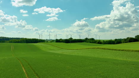 Turbinas-Eólicas-En-Un-Día-Soleado,-Erguidas-En-Un-Vasto-Campo-Verde-Con-Cielos-Azules-Y-Nubes-Dispersas