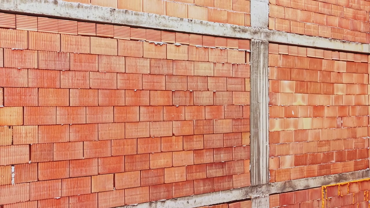 Industriële bakstenen muur als achtergrond. Gedetailleerd beeld van gestructureerd beton en baksteenconstructie. Een gedetailleerde opname toont onafgewerkte constructie met kleibakstenen en structurele ondersteuningen.