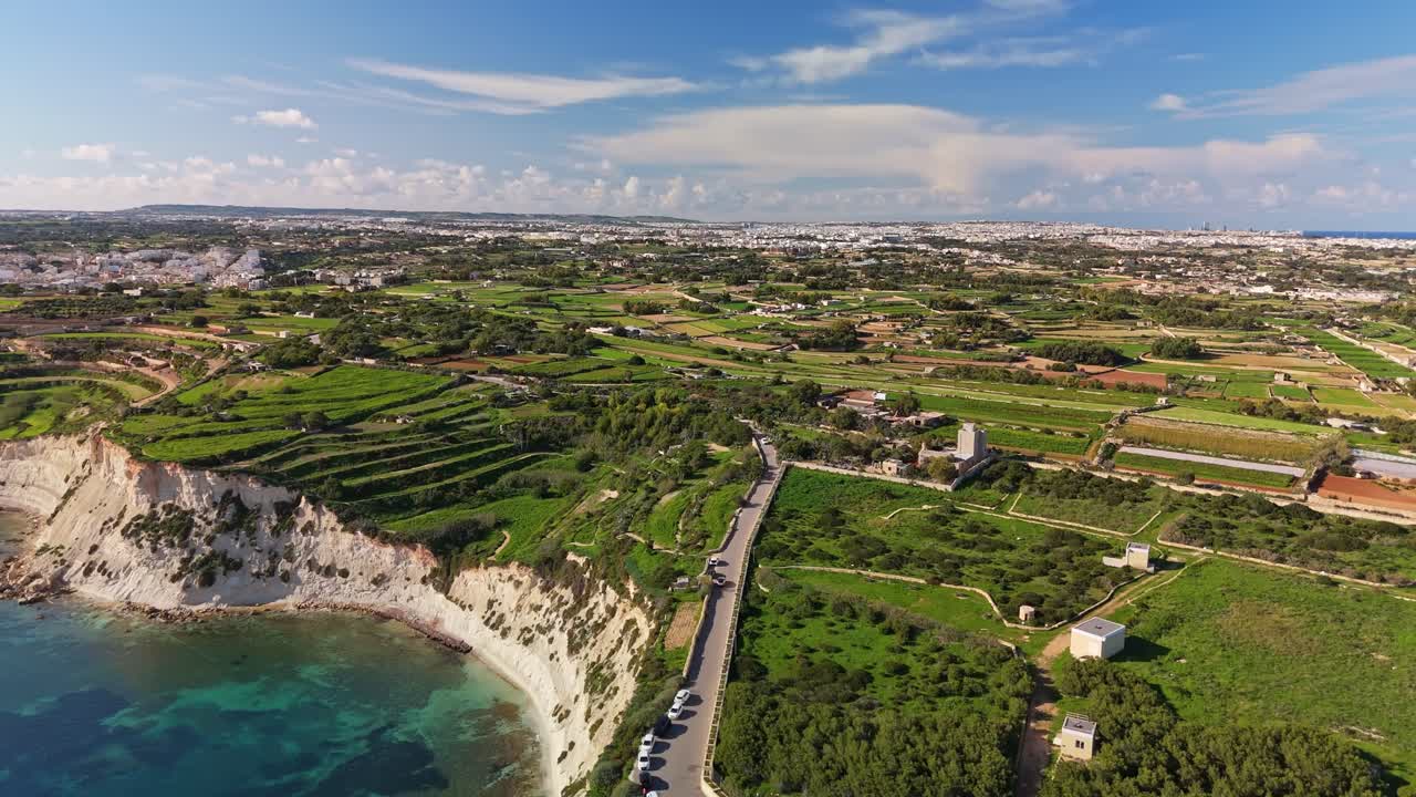 Storslået luftfoto langs Maltas sydlige kyst, der fanger frodige grønne landskaber, dramatiske klipper og turkisblåt middelhavsvand nær Triq Xrobb L-Għaġin under en klar, blå himmel