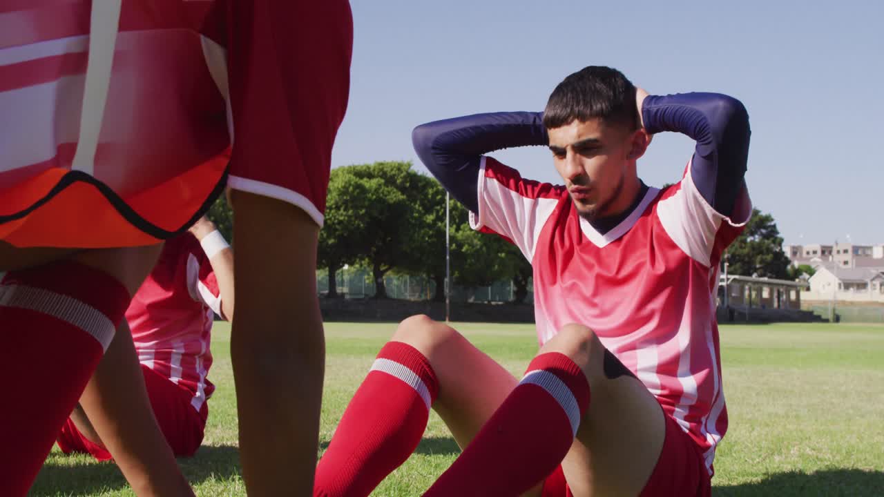 남성 축구 선수 들 의 다양한 그룹 이 경기장 에서 몸 을 따뜻 하게 하고, 앉아서 운동 을 하는 영상