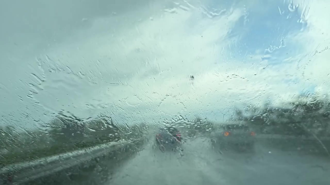 Forte pioggia cade su un'autostrada vista dal parabrezza di un'auto con i tergicristalli in movimento durante una tempesta in un'area urbana.