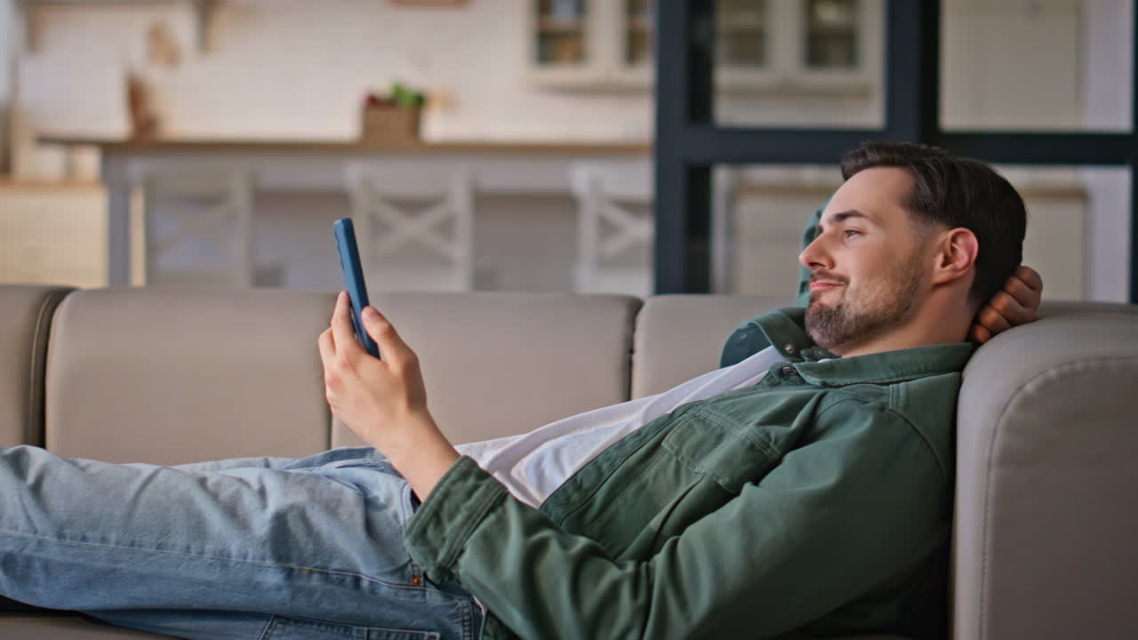 Relaxed man watching greenscreen smartphone lying comfortable home couch closeup