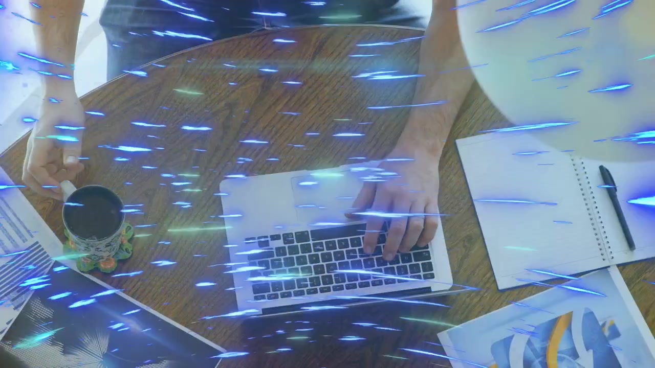 Uomo a una postazione tecnologica che usa un laptop, la mano sospesa che poi afferra una tazza, sorseggiando mentre una scia blu passa.