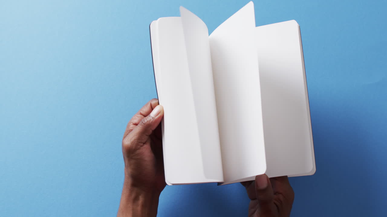 Close up of hand leafing through book with copy space on blue background in slow motion