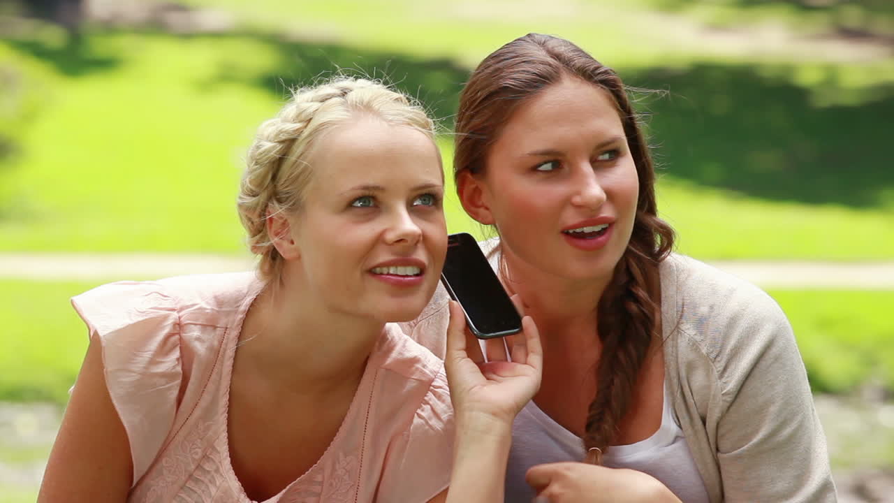 Two shocked women listen to someone on the phone 