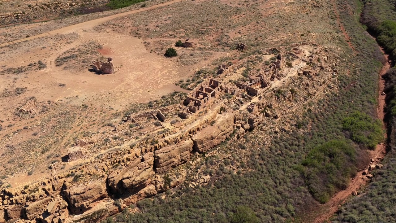 4K UHD dronevlucht die de grimmige isolatie van geruïneerde bakstenen gebouwen in de dorre aarde benadrukt. Vervagende paden leiden door de skeletachtige overblijfselen van deze spookachtige, verlaten klifbuitenpost