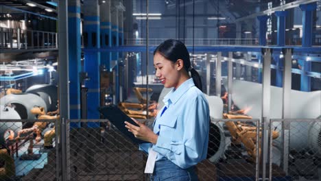 vista lateral de una trabajadora profesional asiática de pie con su tableta en el centro de la fábrica de turbinas eólicas, revisando su tableta con meditación