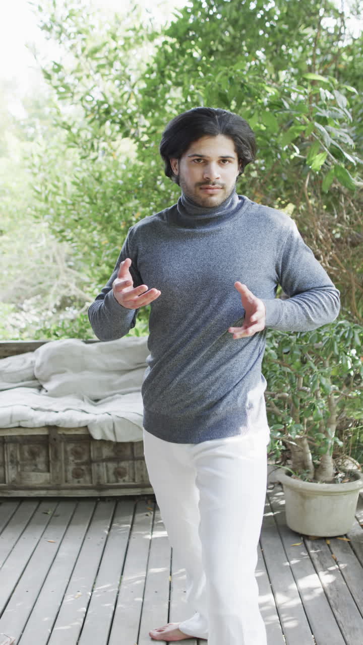 Vertical video of biracial man practicing yoga on terrace in sunny nature, slow motion