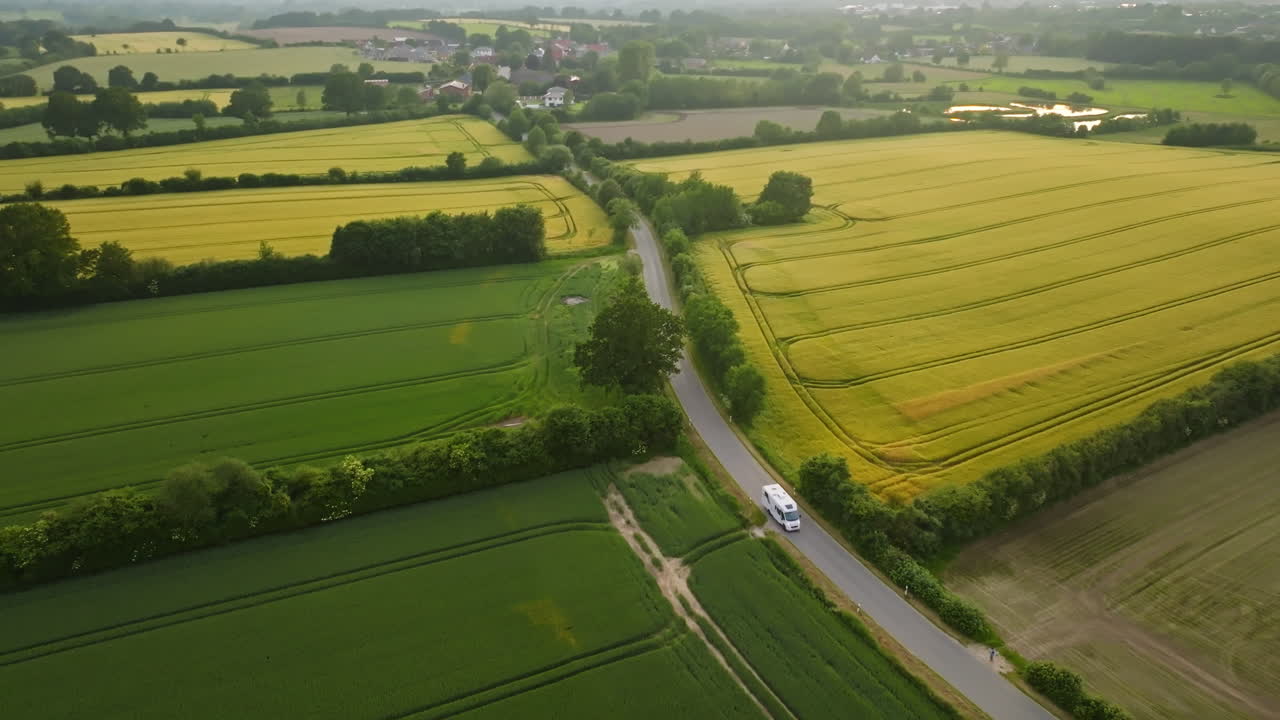 Drone tracking a RV driving between colorful rapeseed farmlands, sunny evening