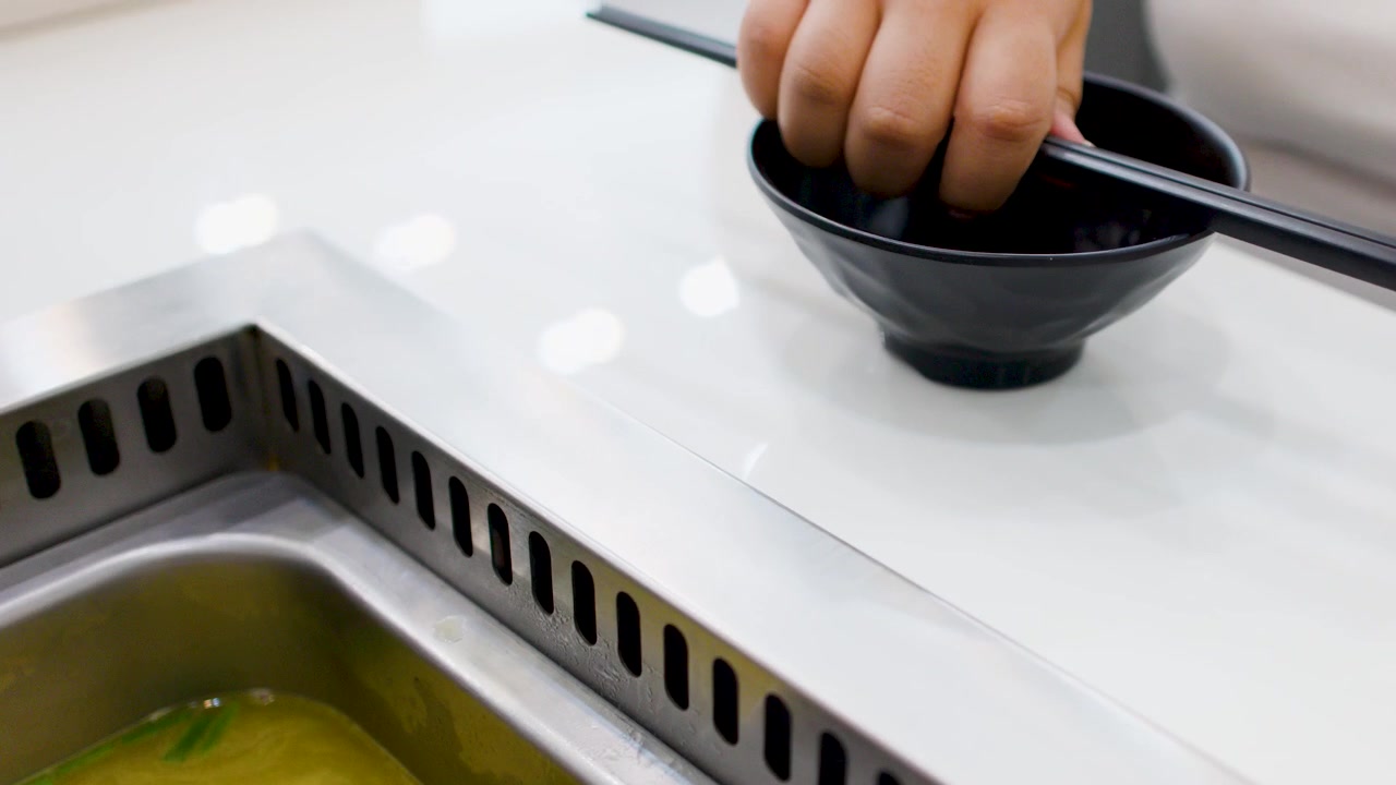 Close-up shot of hands placing a black bowl and chopsticks beside a boiling hot pot