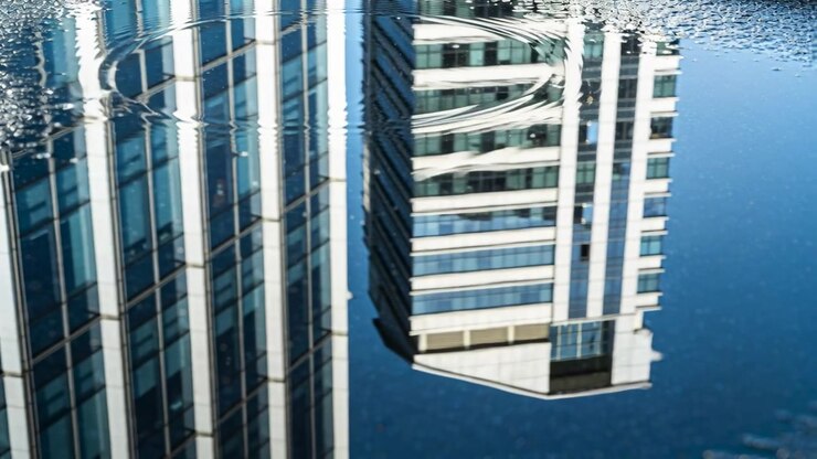 Riflessi mutevoli di torri gemelle che reagiscono a un'increspatura al centro-sinistra in una pozzanghera della piazza, increspandosi verso l'esterno.