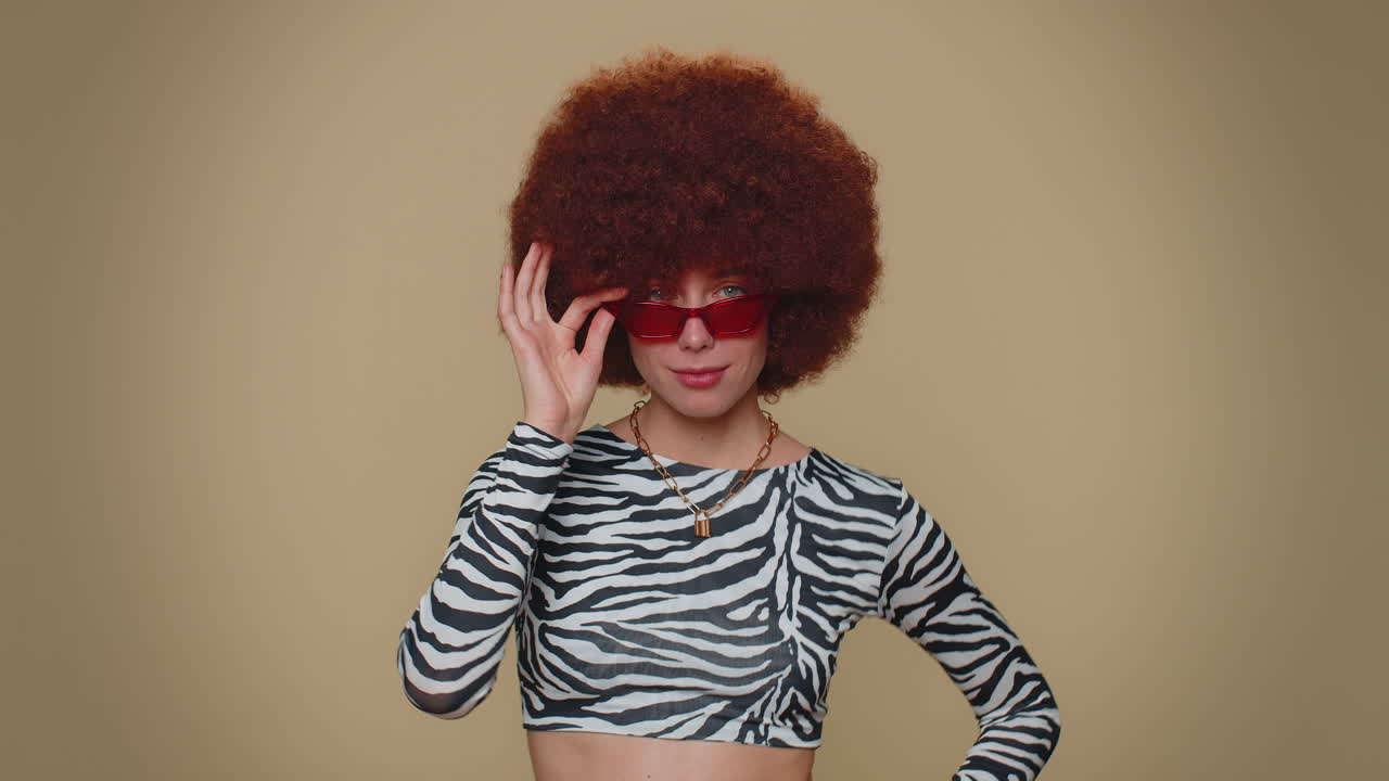 Portrait of seductive pretty young woman with brown lush wig wearing sunglasses, charming smile
