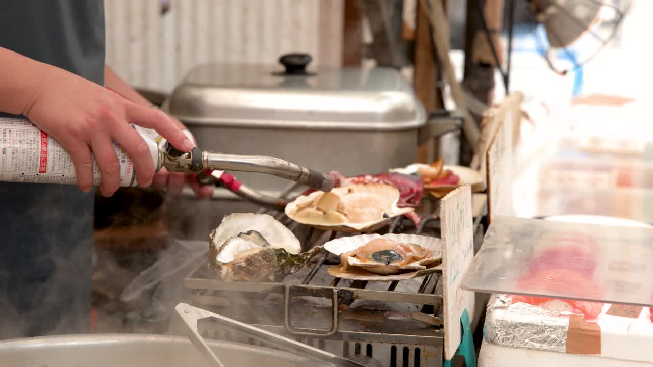 Close-up shot of a vendor using a blowtorch to grill oysters and scallops in Tokyo