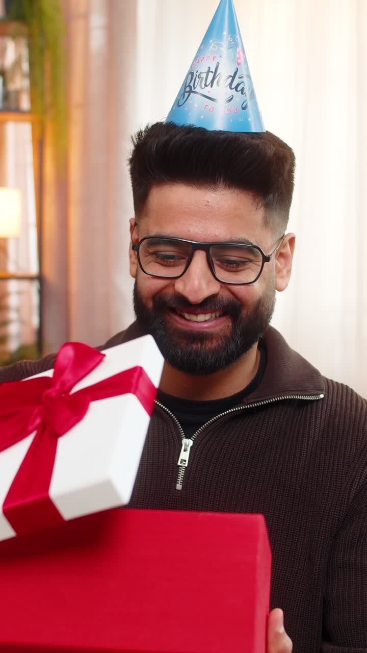 Indian man on sofa opens birthday gift with smile showing joy and surprise in cheerful celebration