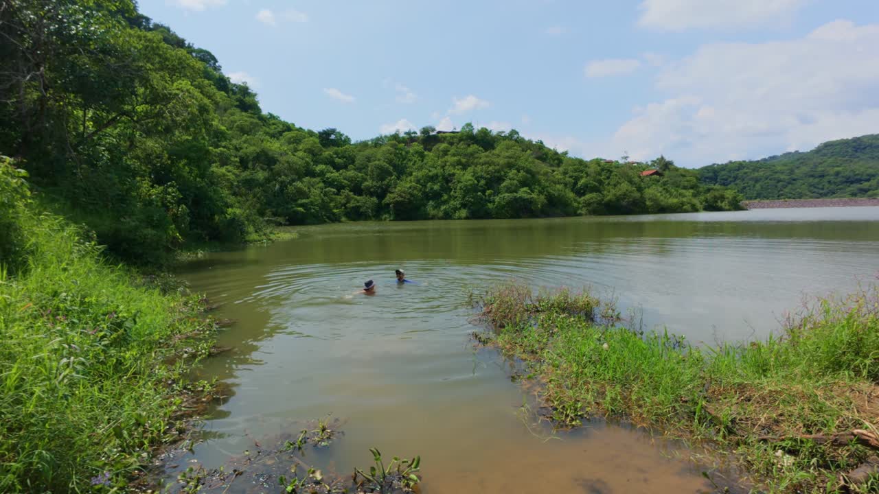 Nadadores disfrutando de la Presa El Carrizo en Jalisco, México. El sereno lago, enmarcado por una exuberante vegetación bajo un cielo azul despejado, crea una atmósfera tranquila y refrescante.