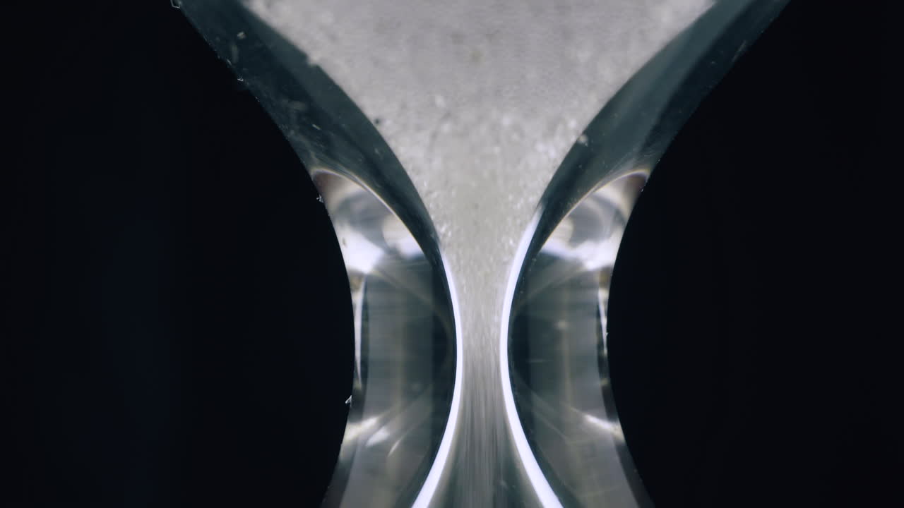 glowing sand pours down in traditional hourglass on black