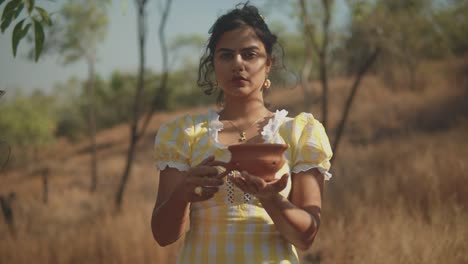 Hispanic-woman-in-yellow-Sevilla-dress-holds-old-clay-teapot,-static-shot