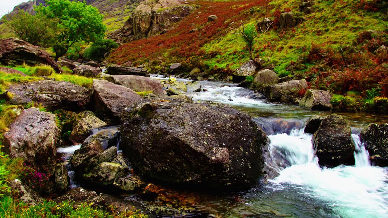 un pequeño arroyo fluye a través de un hermoso paisaje rocoso de colores en snowdonia