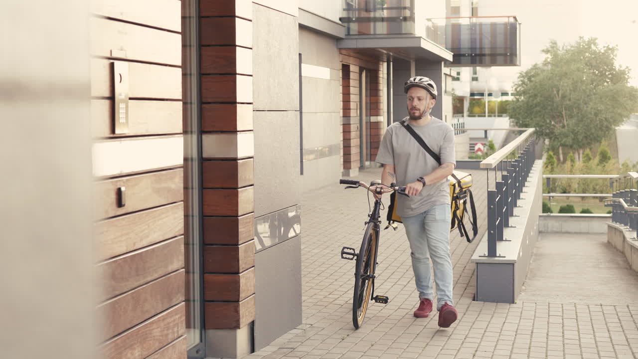 열 배낭을 착용한 음식 배달원은 고객과 고객을 위해 배달하기 위해 건물 입구 옆에 자전거를 주차합니다.