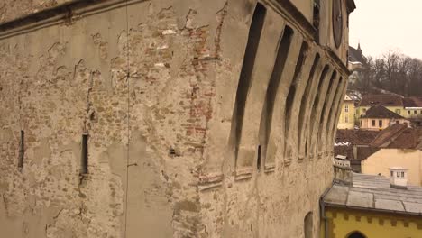 a drone shot, with pedestal upward motion, capturing the partially ruined side of sighisoara clock tower on an afternoon