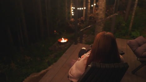 woman sitting by a campfire in the forest at night