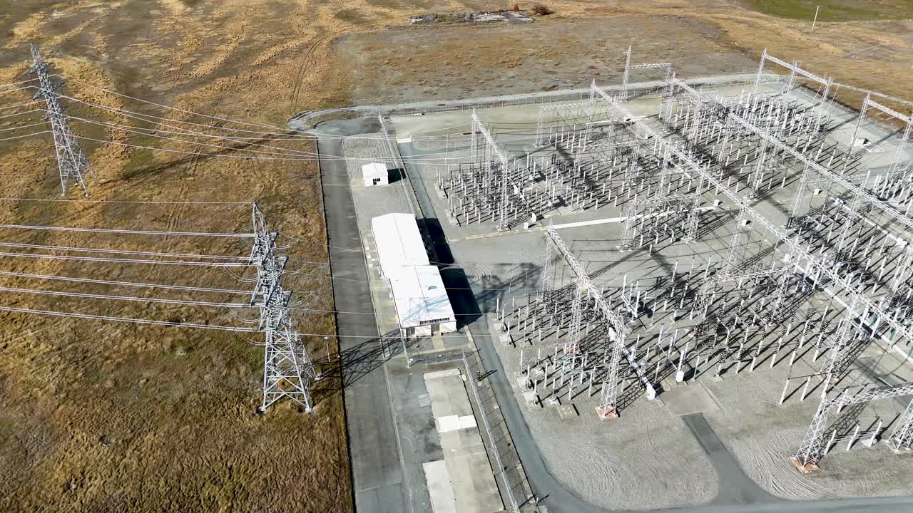 Drone footage captures a sprawling electrical substation at Lake Tekapo, showcasing intricate power lines and transformers under clear skies