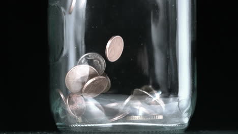 many coins pouring into glass jar close up