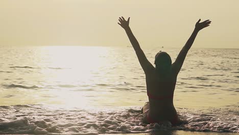 silueta de una mujer levantando las manos al sol en una playa tropical