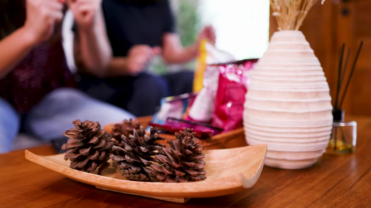 Primer plano de piñas en una bandeja de madera con personas difuminadas comiendo aperitivos detrás de ellas.