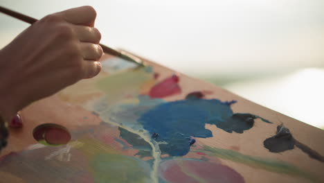 a close-up view of a female hand delicately mixing paints on a palette with a small paintbrush. the soft light enhances the artistic process, capturing the motion and subtlety of blending colors