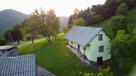 volando hacia una pequeña casa de vacaciones en el campo en las colinas entre la naturaleza verde con el sol en el fondo