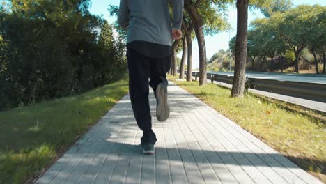 a runner dressed in a grey outfit running on a tree-lined sidewalk while running a marathon