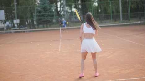 a young woman practicing tennis on an outdoor court with a coach. the coach provides guidance as the player works on her technique, perfecting her strokes in an athletic training session.