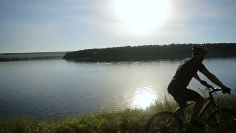 young man with bike at sunset. view of cyclist riding mountain bike on rocky trail at sunset