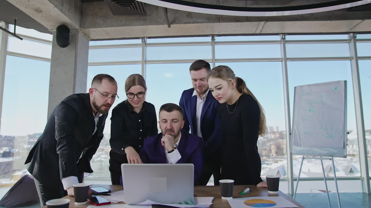 Sharing ideas and finding solutions in teamwork. Business team stand around boss and look at his laptop, talk and smile.