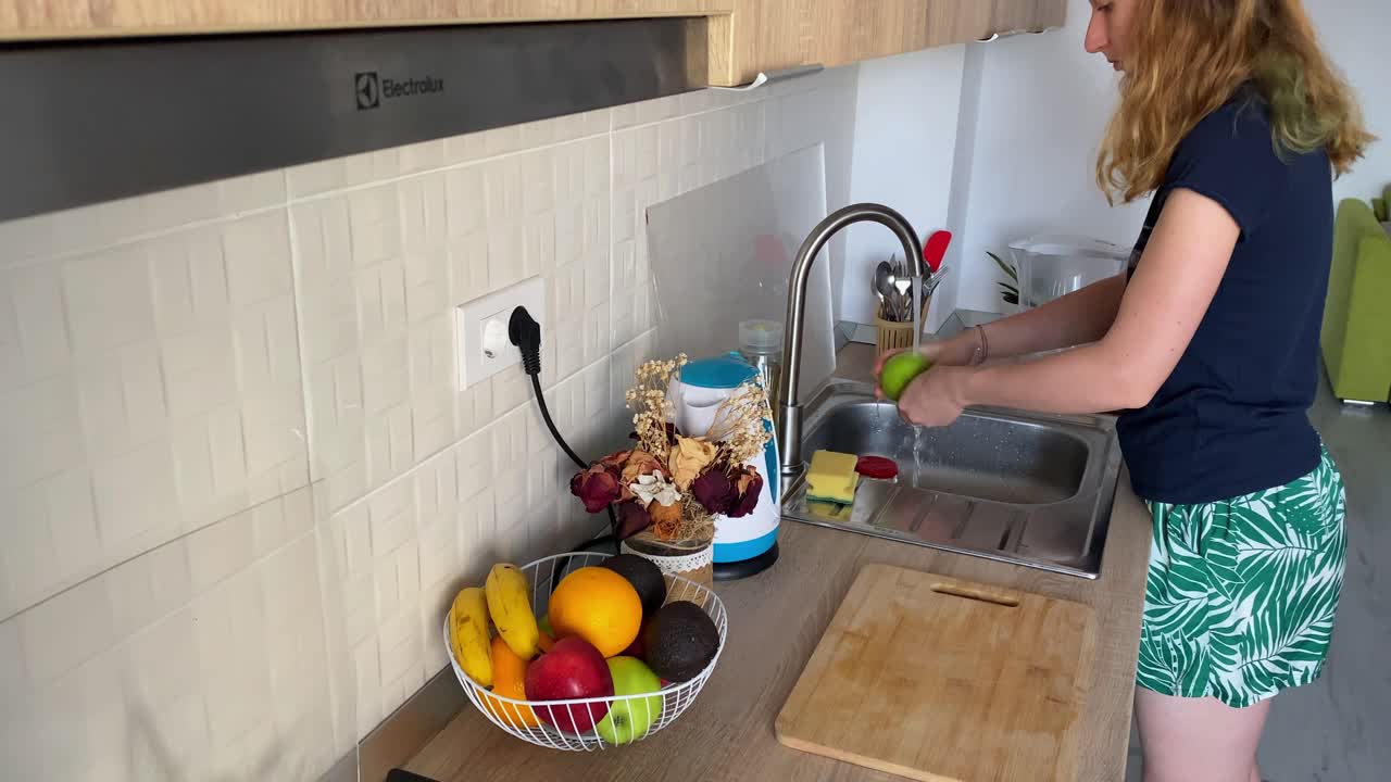 Mujer lavando una manzana en el fregadero para garantizar una alimentación segura y limpia en casa.