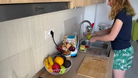 mujer lavando una manzana sobre el fregadero para garantizar una comida segura y limpia en casa