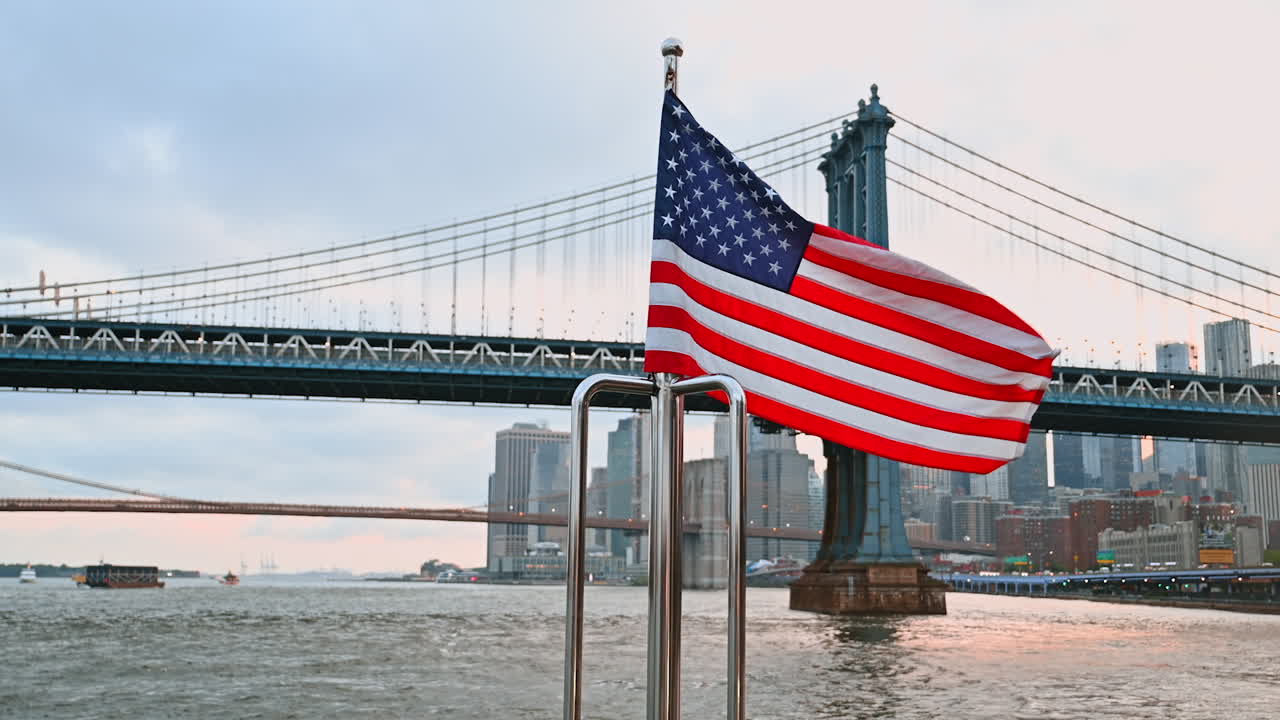 American flag on the metal rail flapping in the wind. The Manhattan Bridge and New York skyline at backdrop