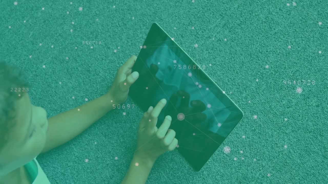 Niño acostado sobre césped verde tocando una tableta que muestra superposiciones de datos de partículas y explorando menús educativos.