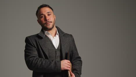 a man in a suit and coat standing in front of a grey background