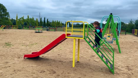 adorable toddler runs up to the slide on the playground. kid goes up by the stairs, sits banging feet and slides down.