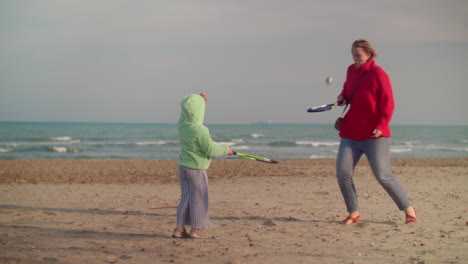 kid and mom playing beach tennis near the sea