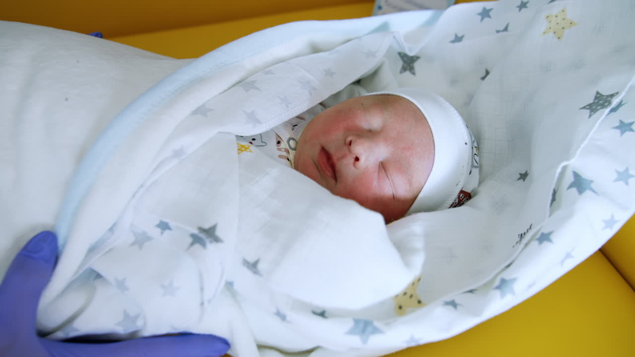 Newborn baby wearing cute cap sleeps peacefully covered in blanket. Close up. Top view.