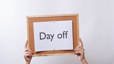 woman's hand shows the paper on board with the word day off in white studio background with copy space