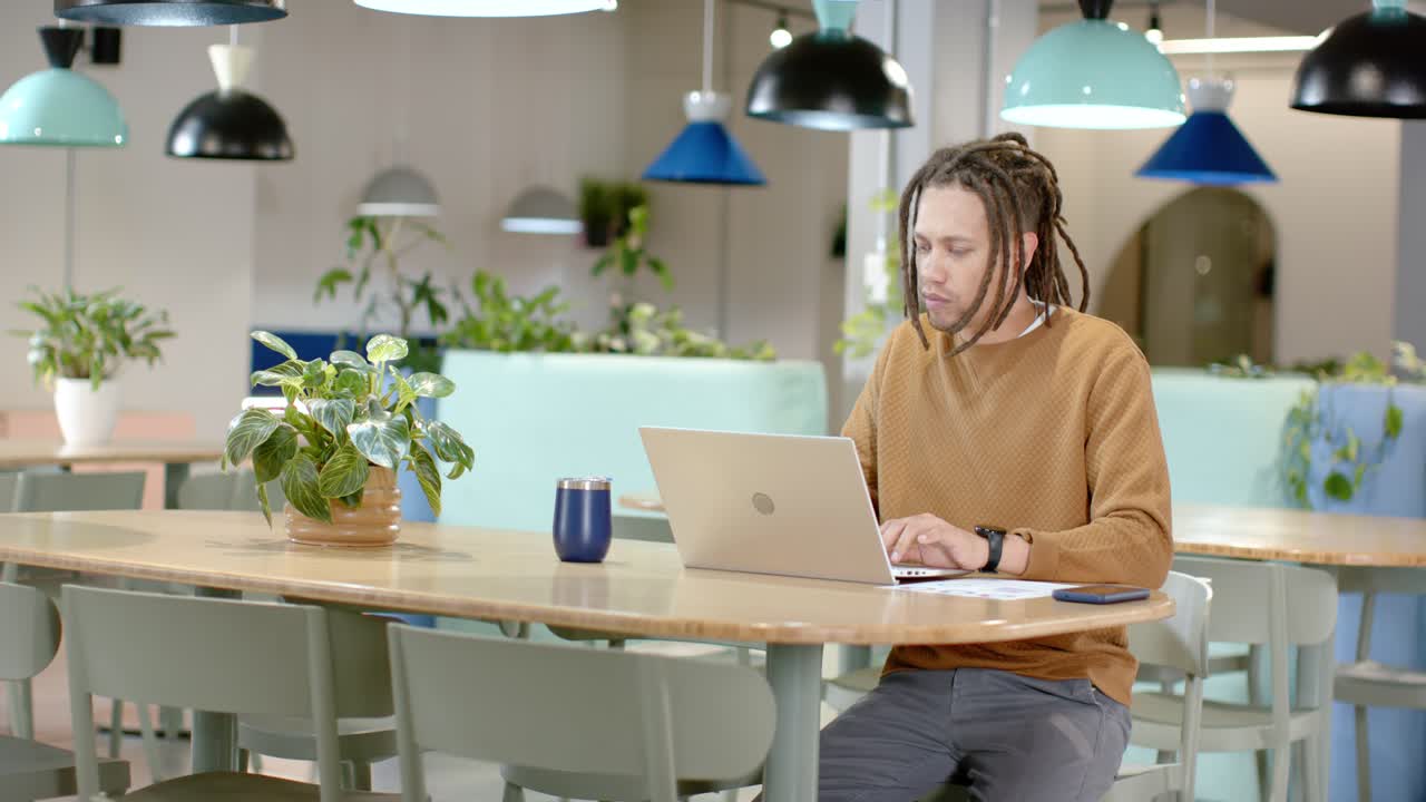 Man scanning paper, leaning, typing on laptop, reviewing notes in coworking space, copy space