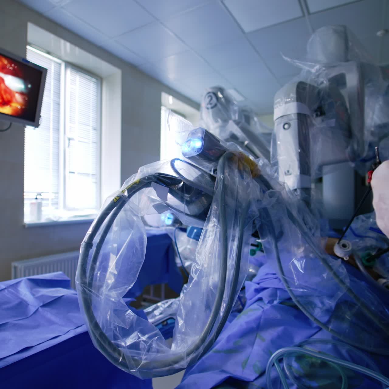 Futuristic arms of Da Vinci robot move in the patient's body. Doctor's hand inserts the instrument into the attached device. Operational procedure is displayed on the monitor