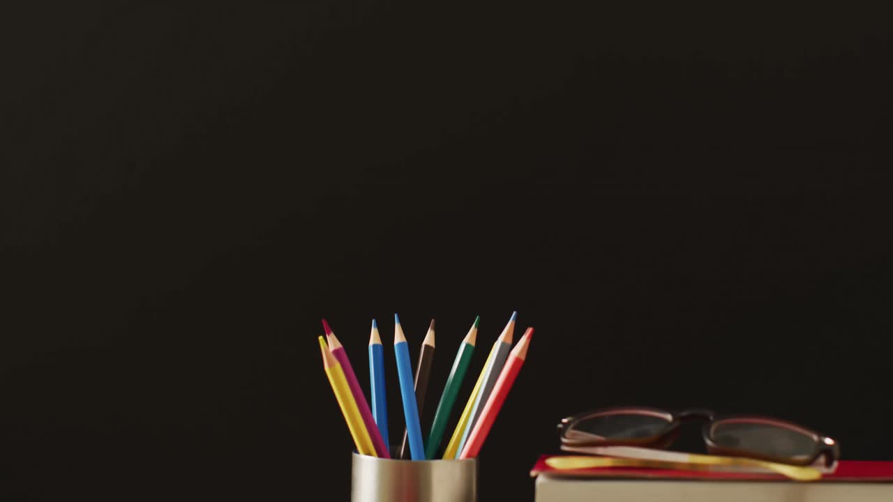 video de una pila de libros, lápices de colores y manzana sobre fondo negro